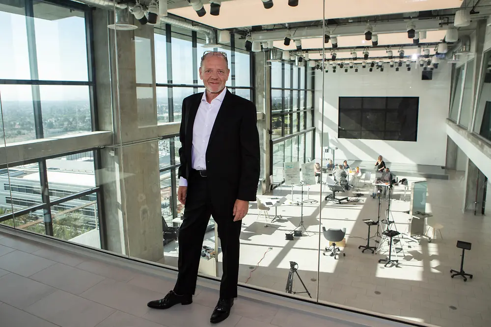 Stefan L. Mund, Regional Head Henkel Beauty Care Professional North America in front of a glass wall with view of a seminar room with people