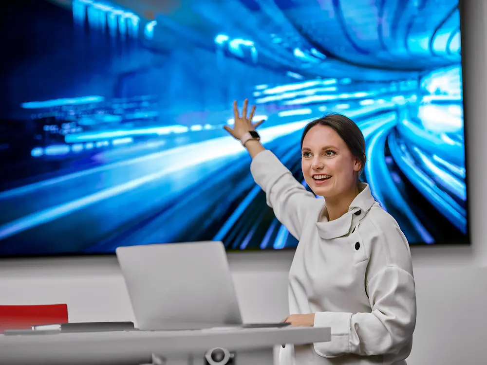 A woman gives a presentation in front of a screen with images symbolizing digitalization.