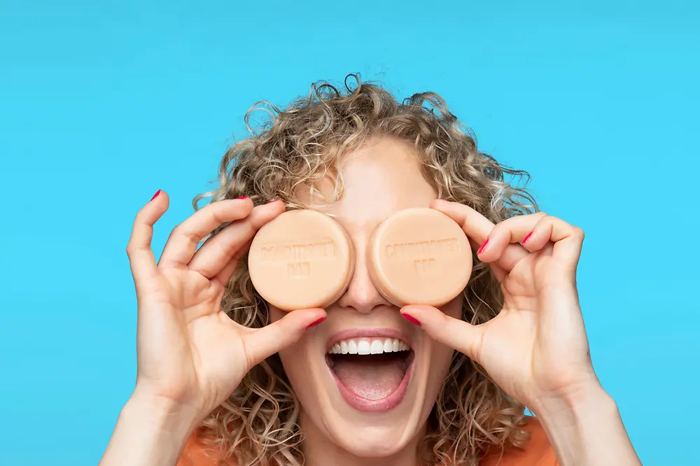 A happy woman holds two Nature Box solid conditioners in front of her eyes.