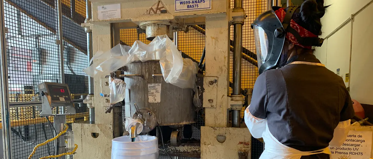 A woman wearing PPE stands in front of a large chemical mixer.