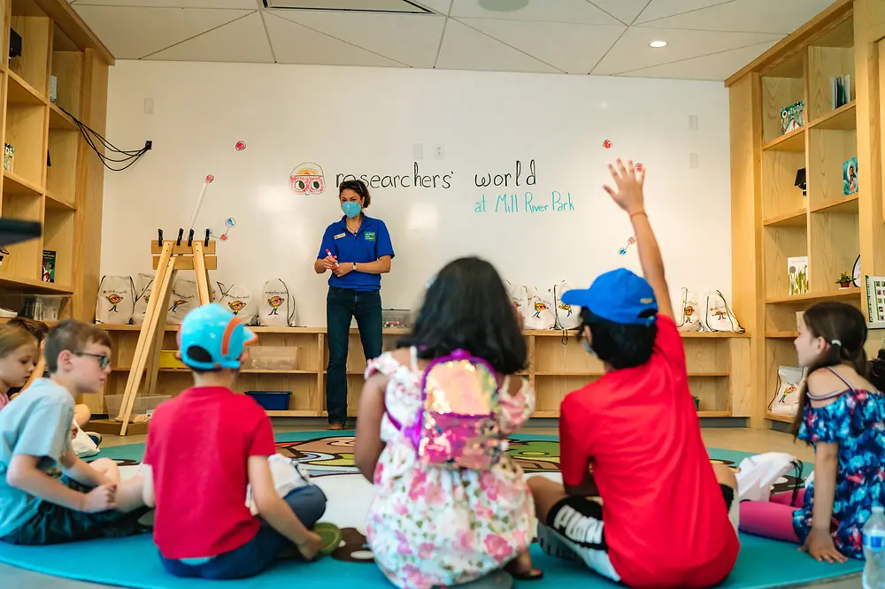 Henkel Researchers’ World instructor talking to children in a semi-circle sitting on the ground in a classroom.