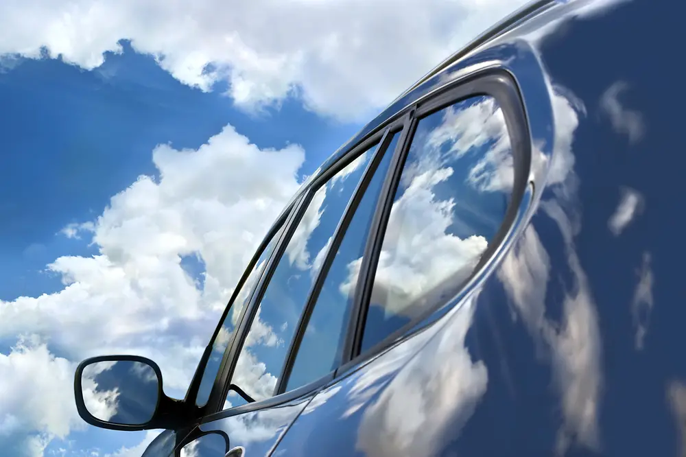 A car with sky and clouds reflecting on surface