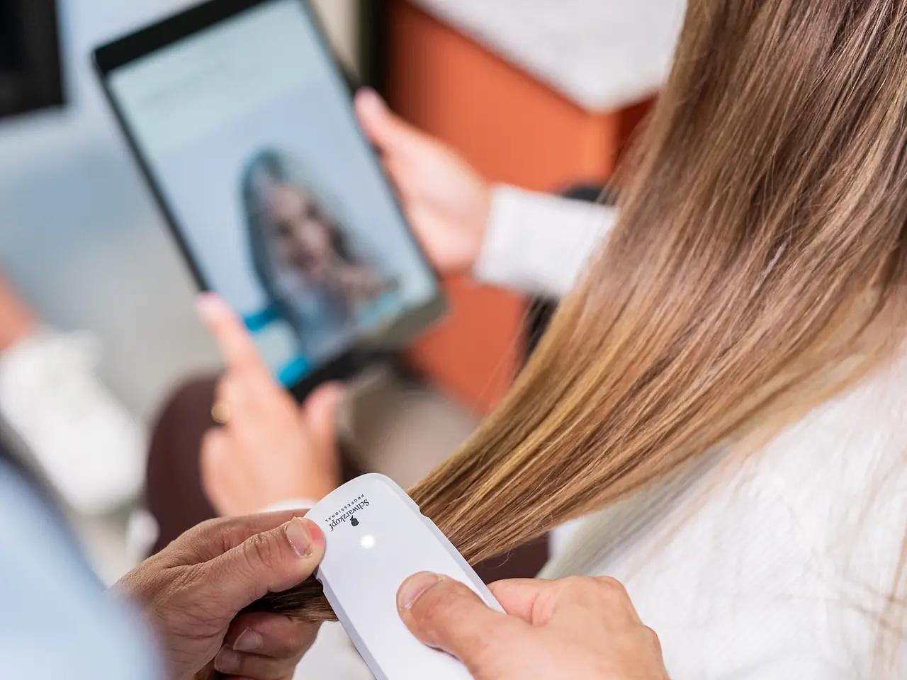 The hairdresser scans the customer's hair with the SalonLab Analyzer while she holds a tablet in her hand.