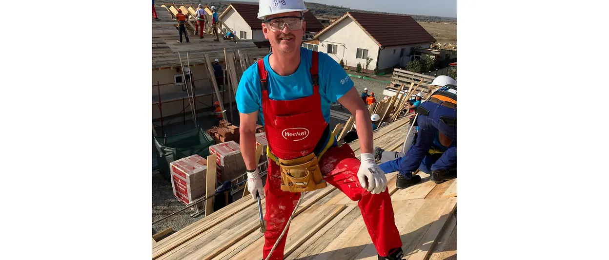 Secured with a belt, Henkel employee Jörg stands on the roof of the unfinished apartment building.