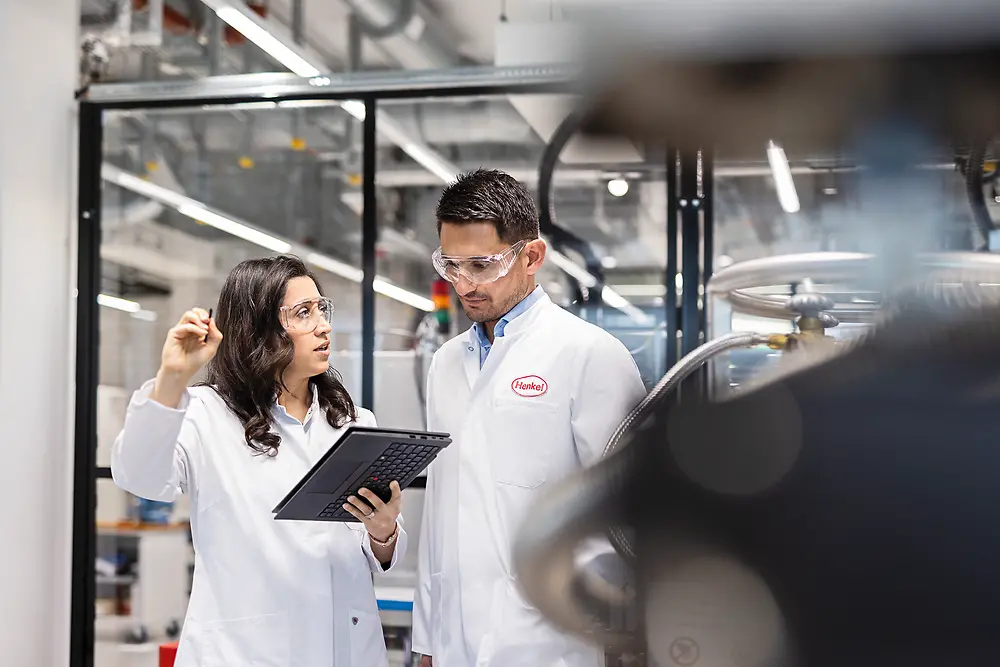 Two lab staff in lab coats discuss a test using a tablet in a laboratory at the Inspiration Center Düsseldorf.