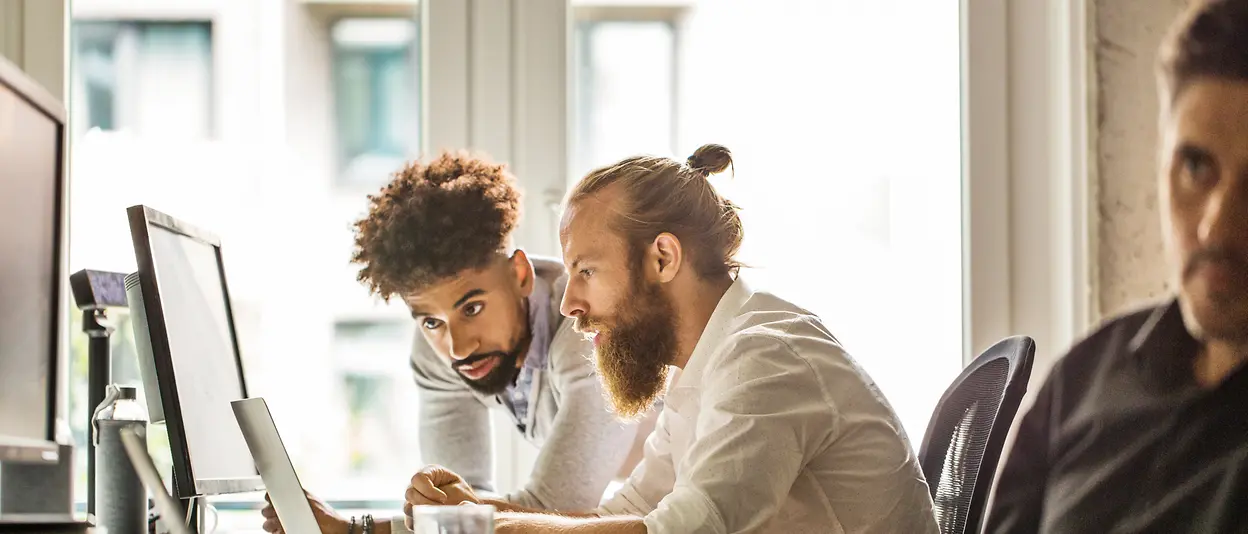 Two men look at the screen of a laptop together an exchange ideas. 