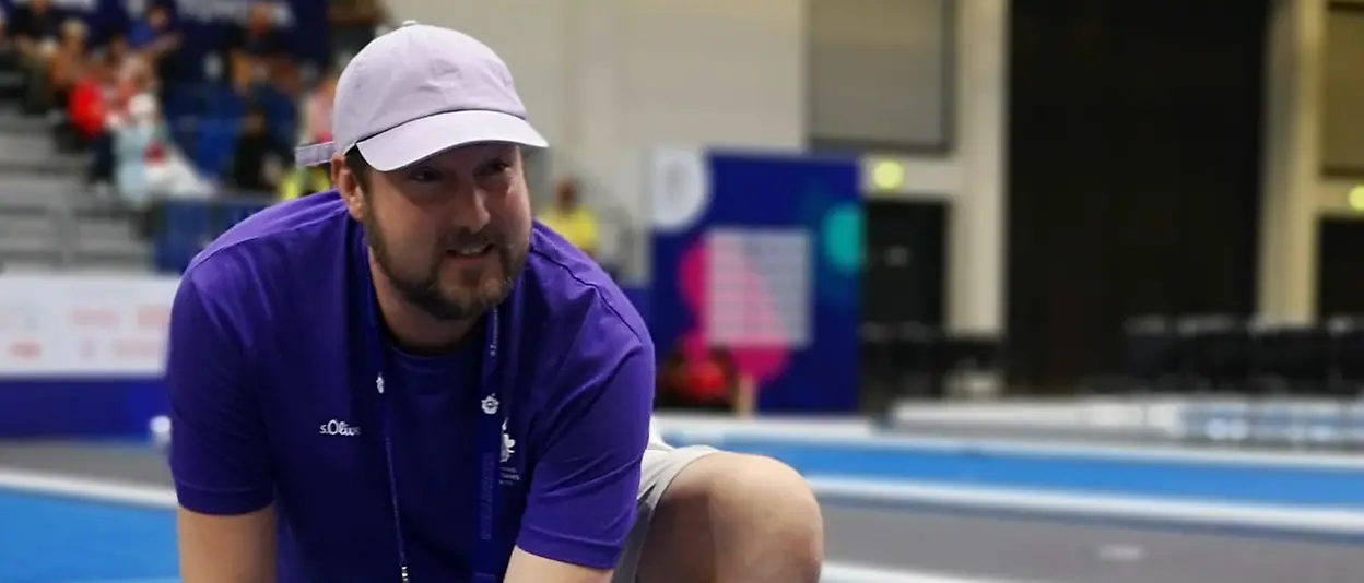 Tobias kneels on the boccia court and is in the process of dismantling it.