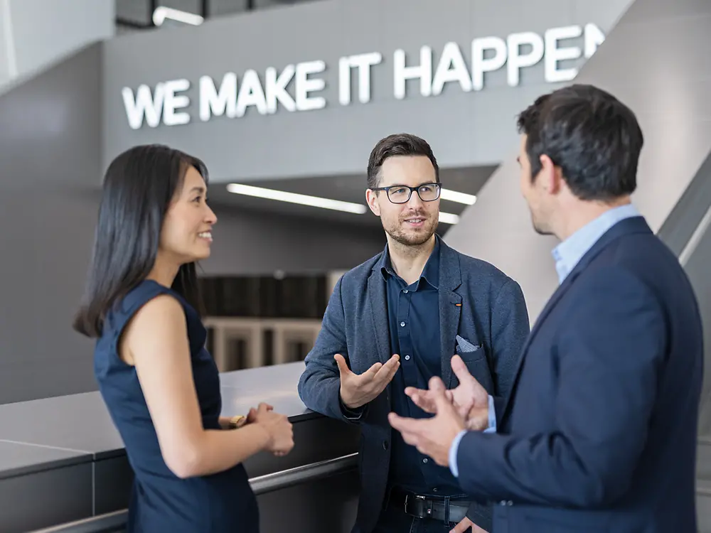 Two customers in the foyer of the Inspiration Center Düsseldorf talking to a customer experience tour guide.