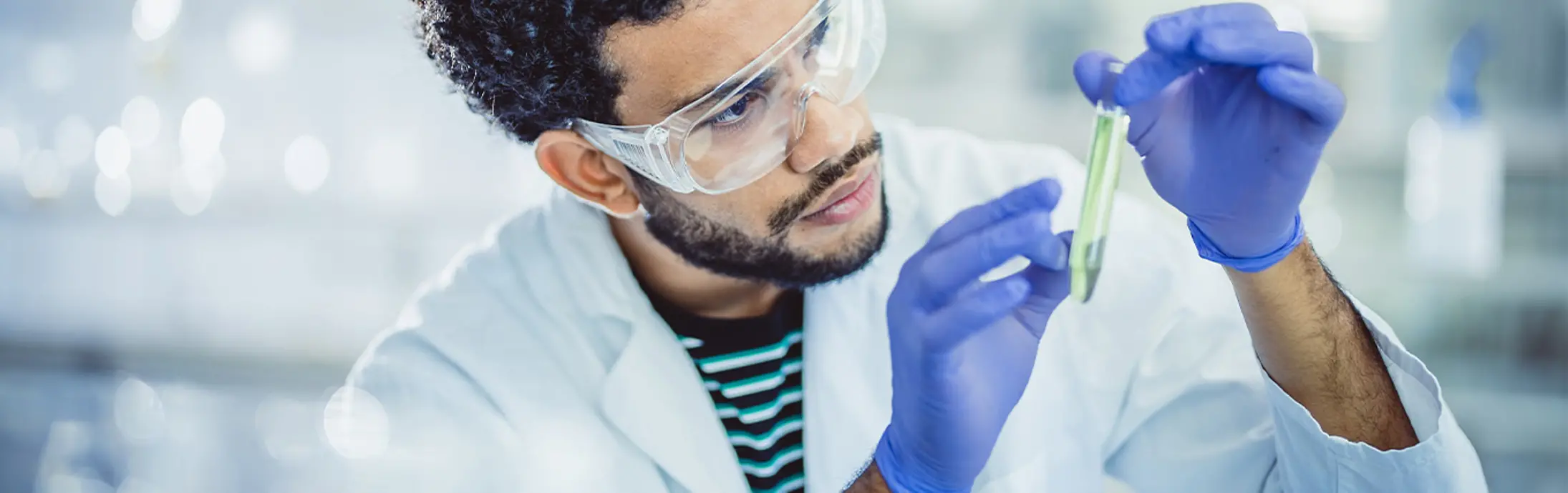 Young researcher in a lab holds and observes a test tube.