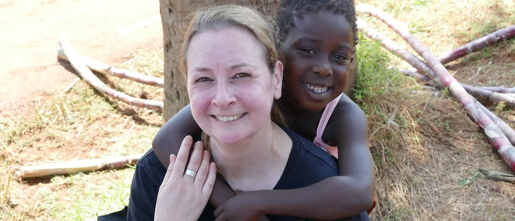 With two children from Sonrise Ministries in her arms, Henkel employee Gabi Haak is leaning against a tree while smiling into the camera.