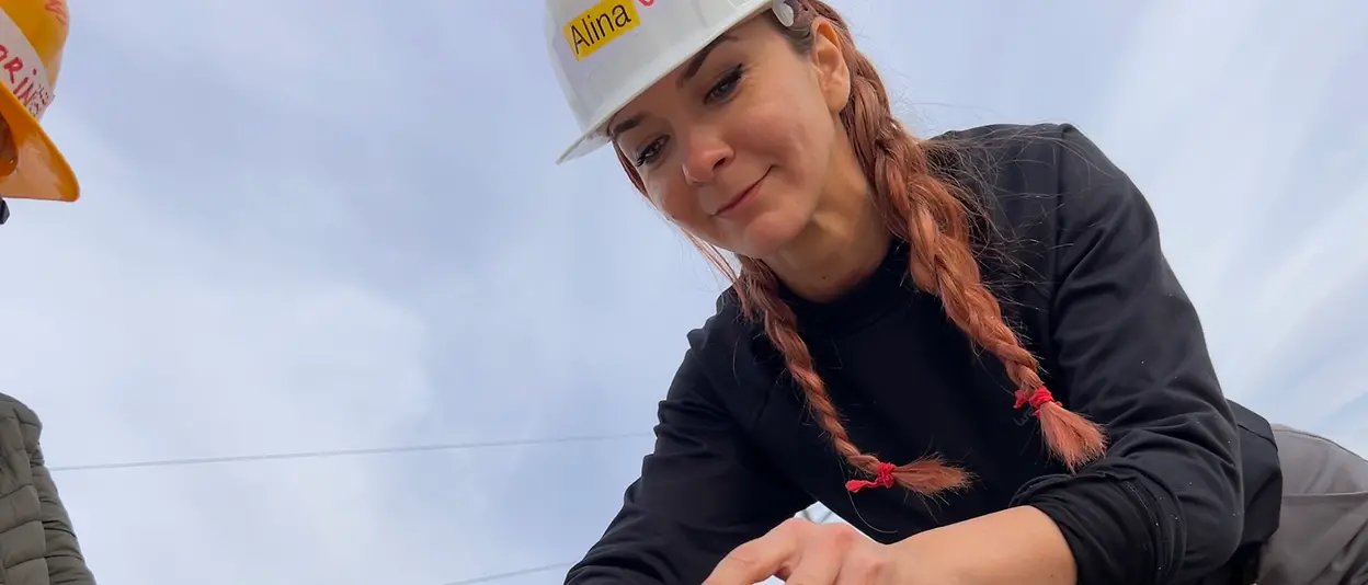 A female volunteer prepares the wooden framework by drilling into the corresponding building components.