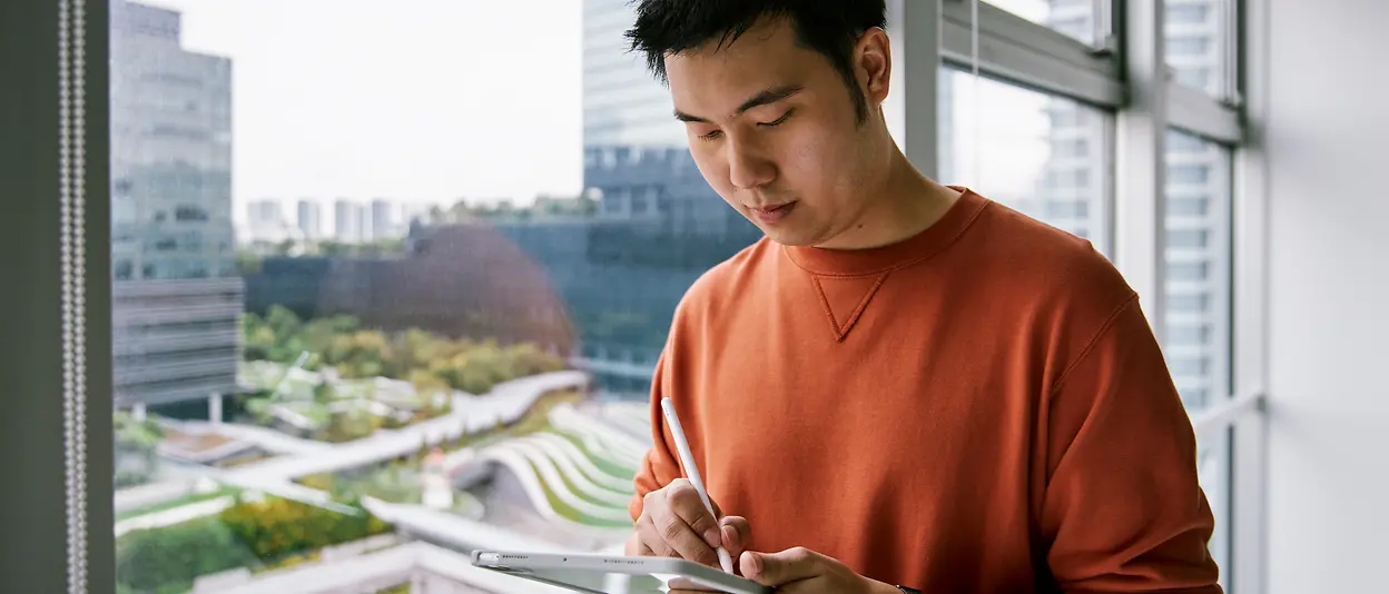 A man standing by a window and writing on a tablet.