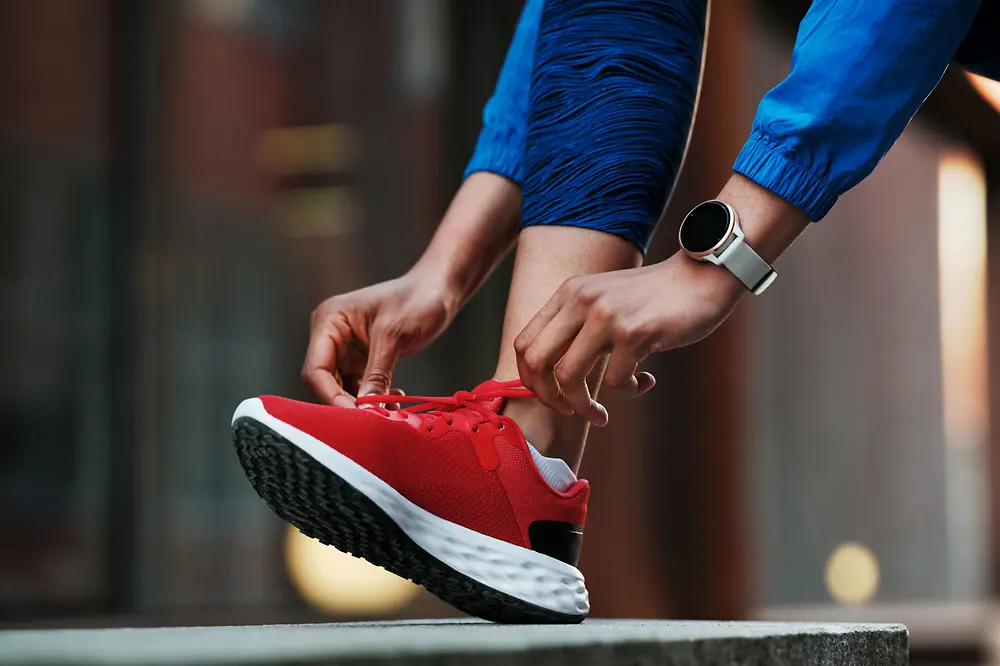 A person lacing up sports shoes bonded with solutions from Henkel Adhesive Technologies and wearing a smartwatch.