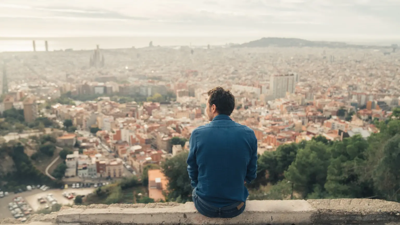 A man sitting on a hill overlooking a city.