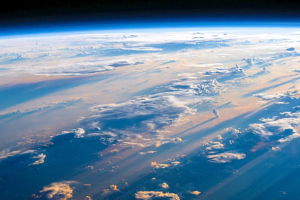 View from the ISS over the Philippine Sea, showing deep blue ocean waters with scattered clouds against the Earth's curved horizon and the blackness of space.