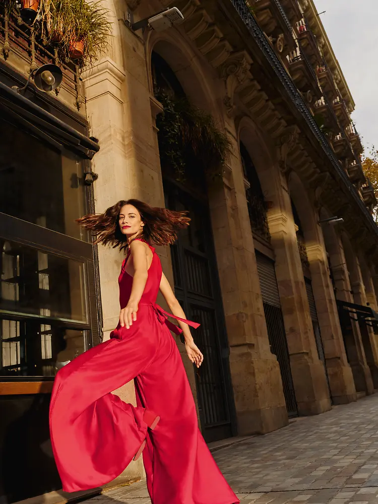 A woman wearing a red flowy jumpsuit is dynamically taking stairs while looking over her shoulder.