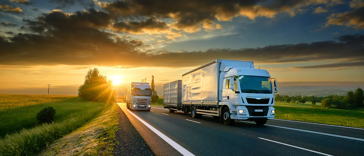 Two trucks driving on a highway with the sunset in the background