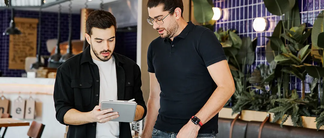 Two colleagues are standing in a modern working environment and looking at something together on a tablet.