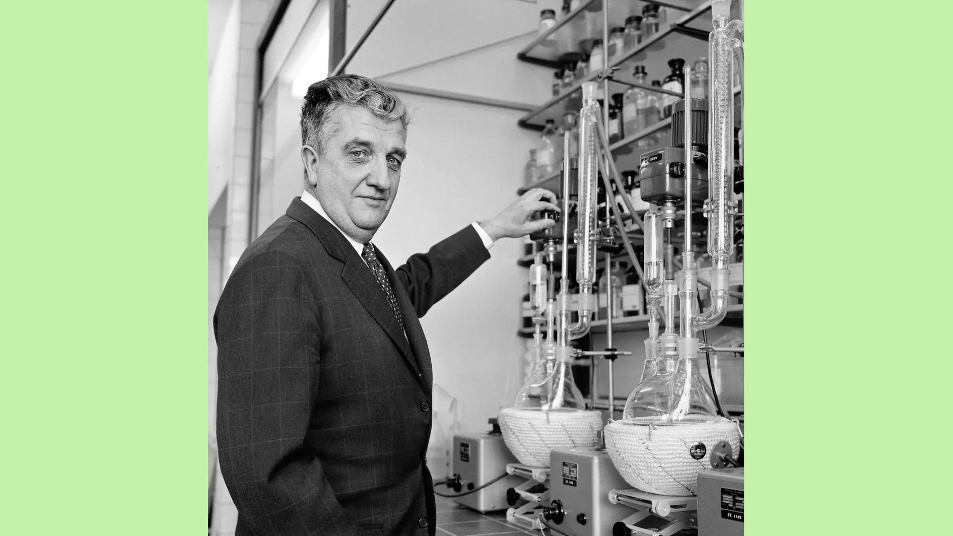 Black and white photo of Dr. Konrad Henkel in one of Henkel’s laboratories. One hand rests on a distiller while the other is casually tucked into his trouser pocket. His gaze is directed straight at the camera taking his picture.