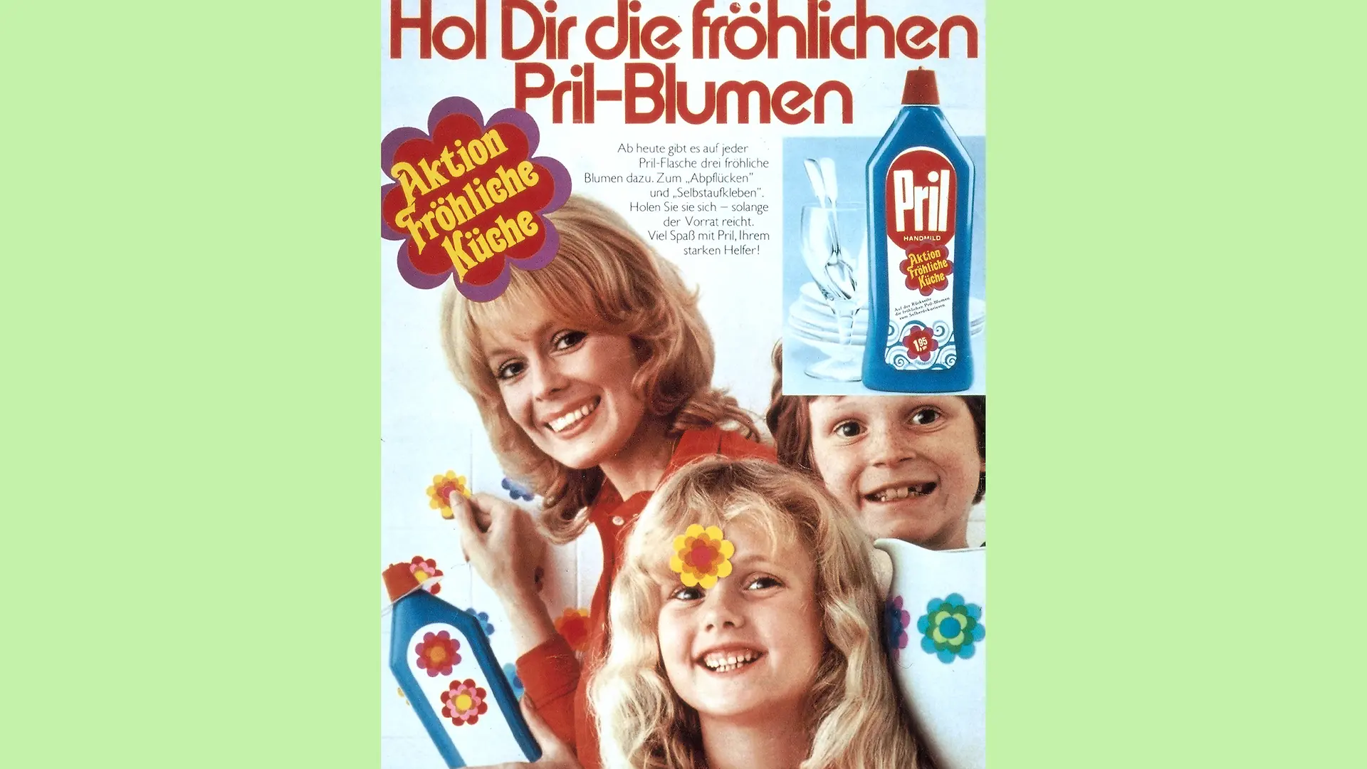 Advertisement for the “ Fröhliche Küche” (Happy Kitchen) campaign with a woman, a girl and a boy. They are all smiling at the camera and standing in front of a white tiled wall. The woman is holding a bottle of Pril with two Pril flowers in her hand and is sticking a third one on the wall. The sentence 