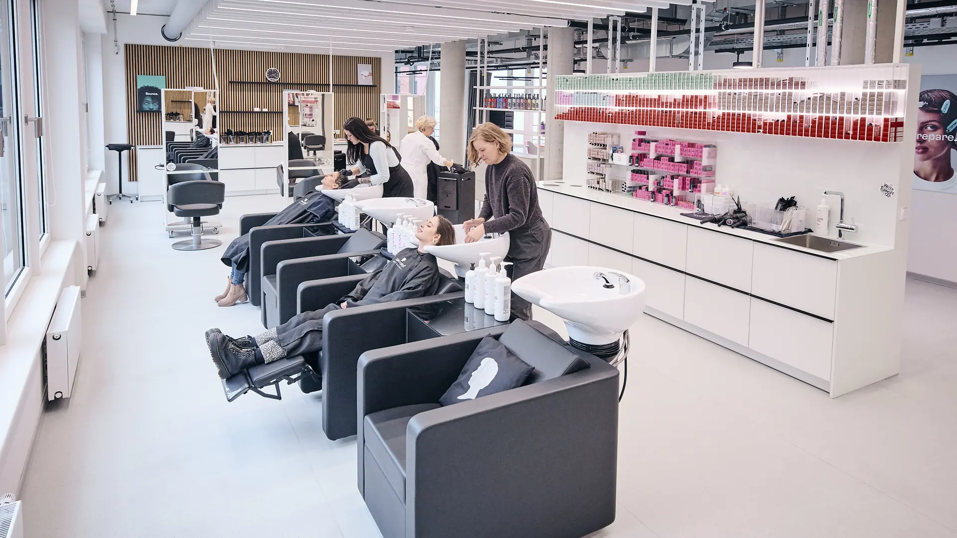 Hair salon with several washbasins. Test customers are sitting in two of the chairs, having their hair washed by two employees.